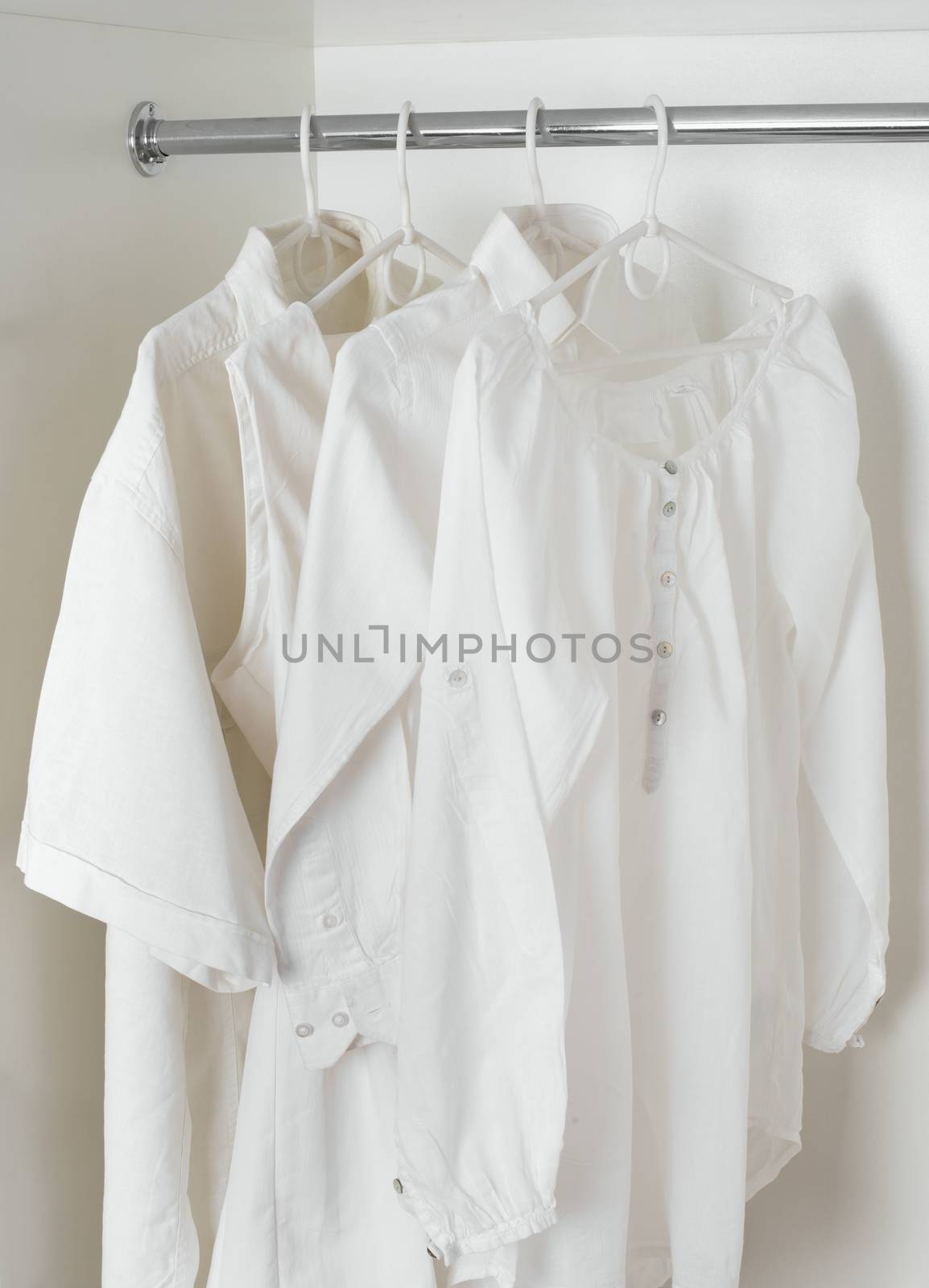 set of white clean ironed clothes hanging on hangers in a white cabinet