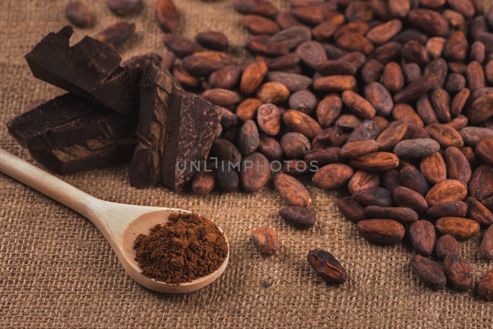 Cocoa beans, wooden spoon with cocoa powder, raw chocolater on sacking