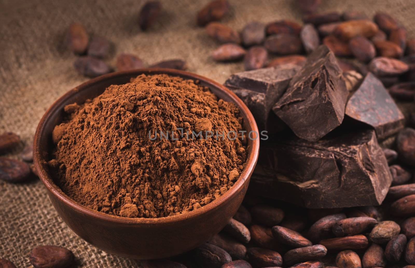 Cocoa beans, clay bowl with cocoa powder, black chocolate on brown sacking