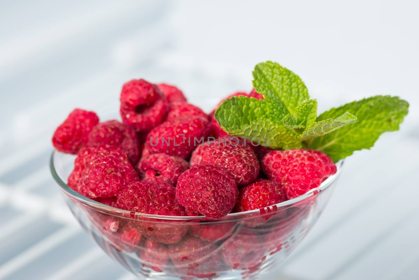 frozen raspberries in a glass piala in the freezer and a sprig fresh of mint