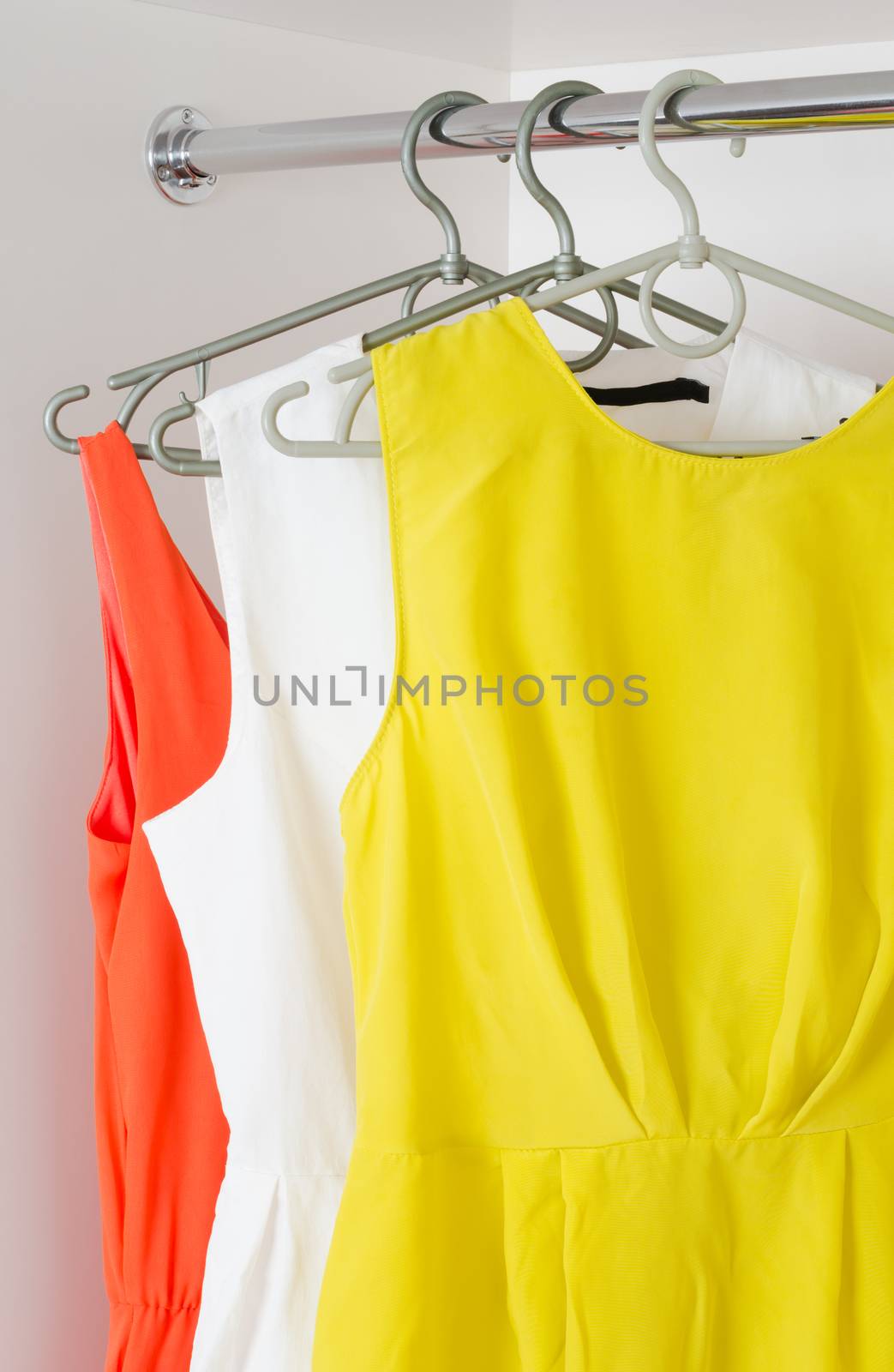 bright colorful  female dresses hanging on coat hange  in white wardrobe