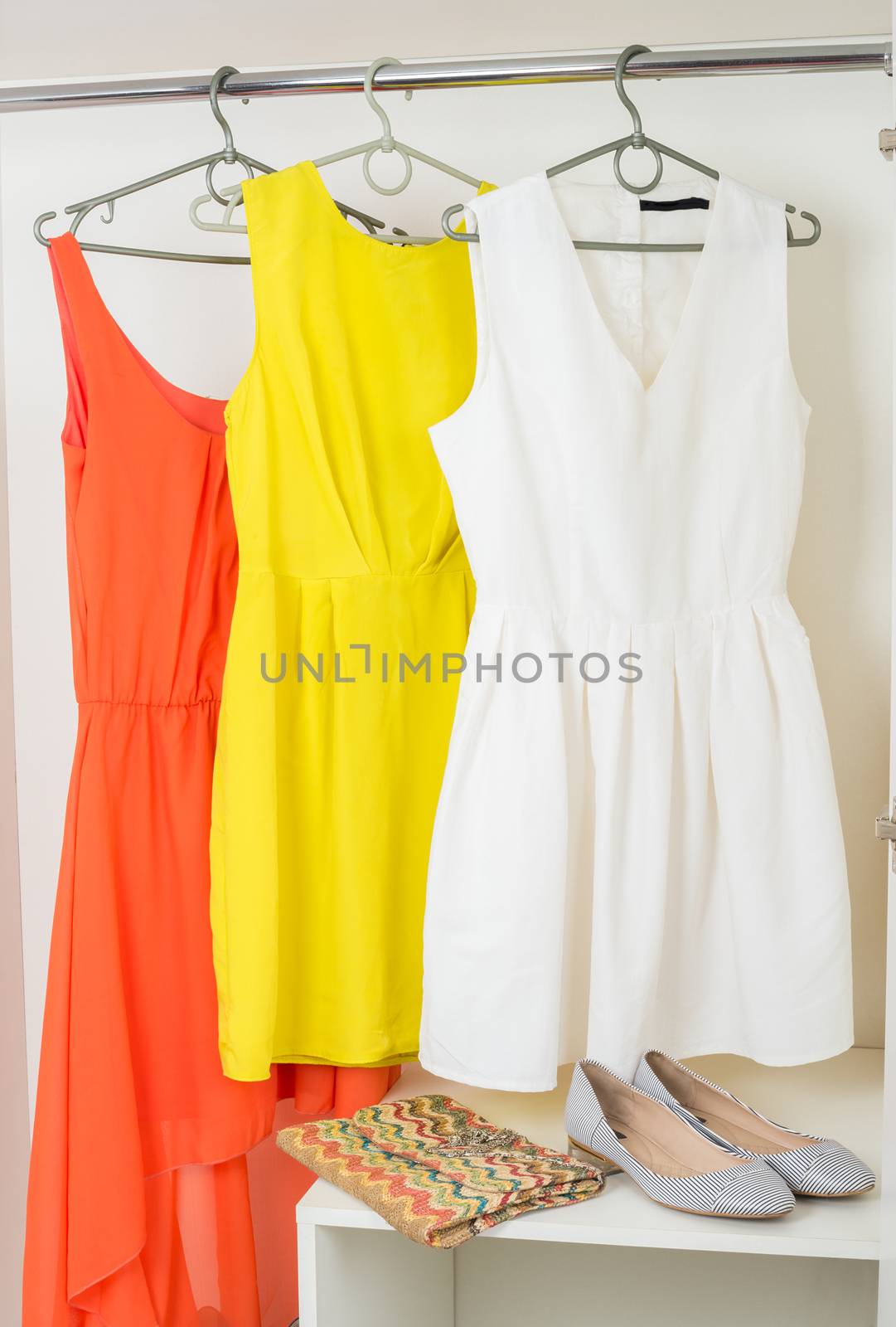 row of  bright colorful female dresses hanging on coat hanger, shoes and handbag in white wardrobe