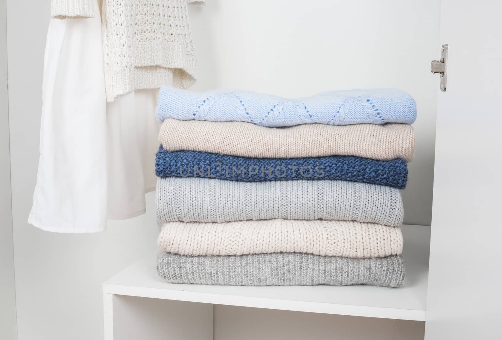  Stack of knitted warm woolen clothes in white wardrobe close up