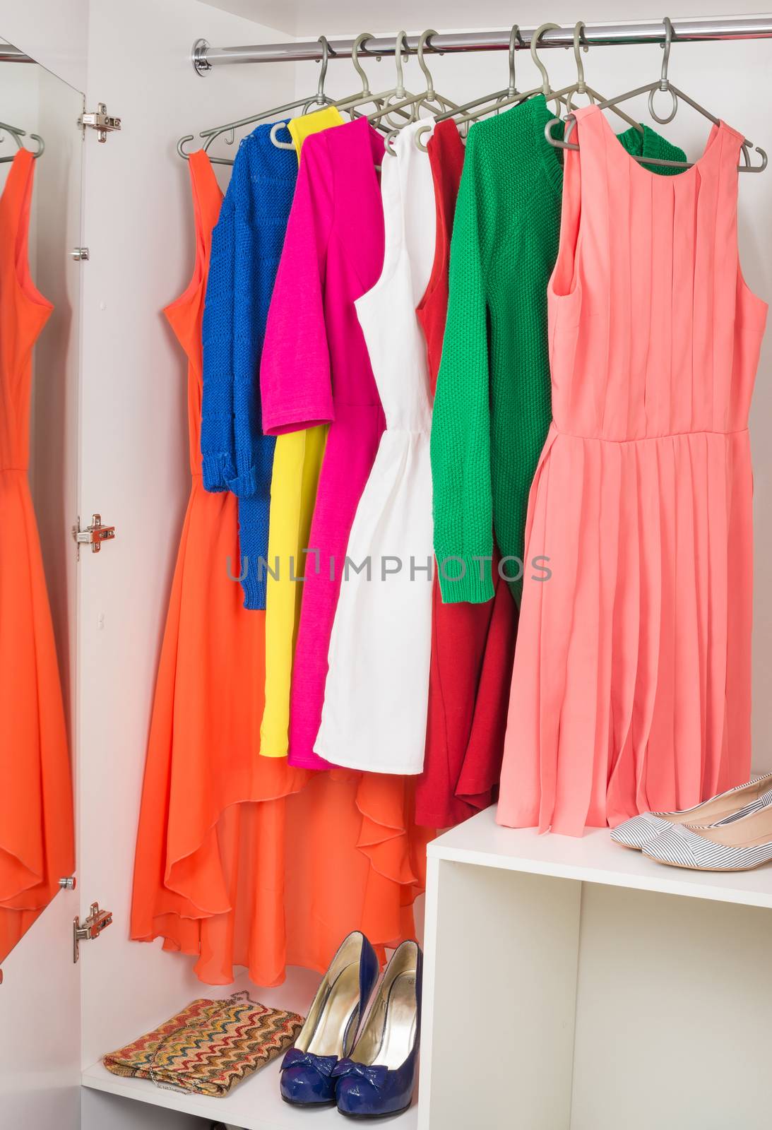 bright colorful female dresses and sweaters  hanging on coat hanger,  shoes and handbag in white wardrobe