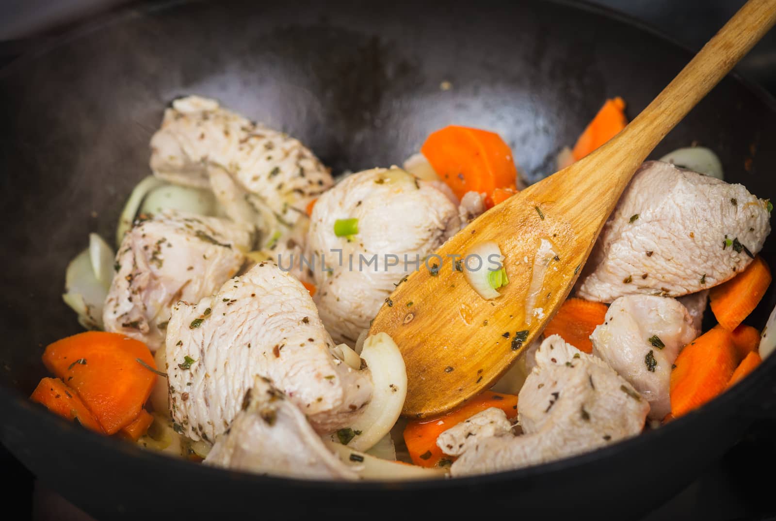 Cooking turkey with vegetables and spices in a frying pan fried minced raw turkey into pieces, chopped carrots, onions and dried herbs, wooden spoon mixing meat