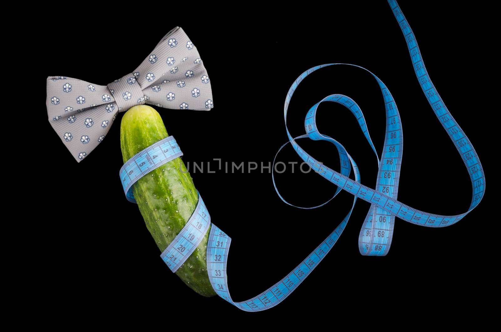 Big cucumber like the penis, centimeter and bow-tie isolated on black background, close-up, top view