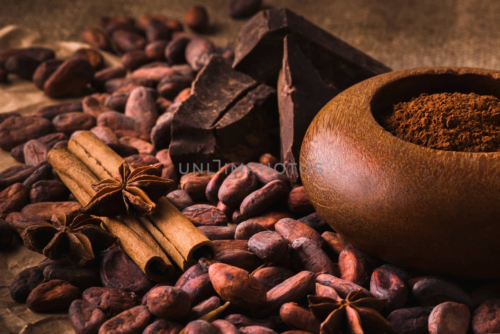 Raw cocoa beans, raw dark   homemade chocolate for raw foodists, cinnamon sticks, star anise and cocoa powder in a wooden bowl