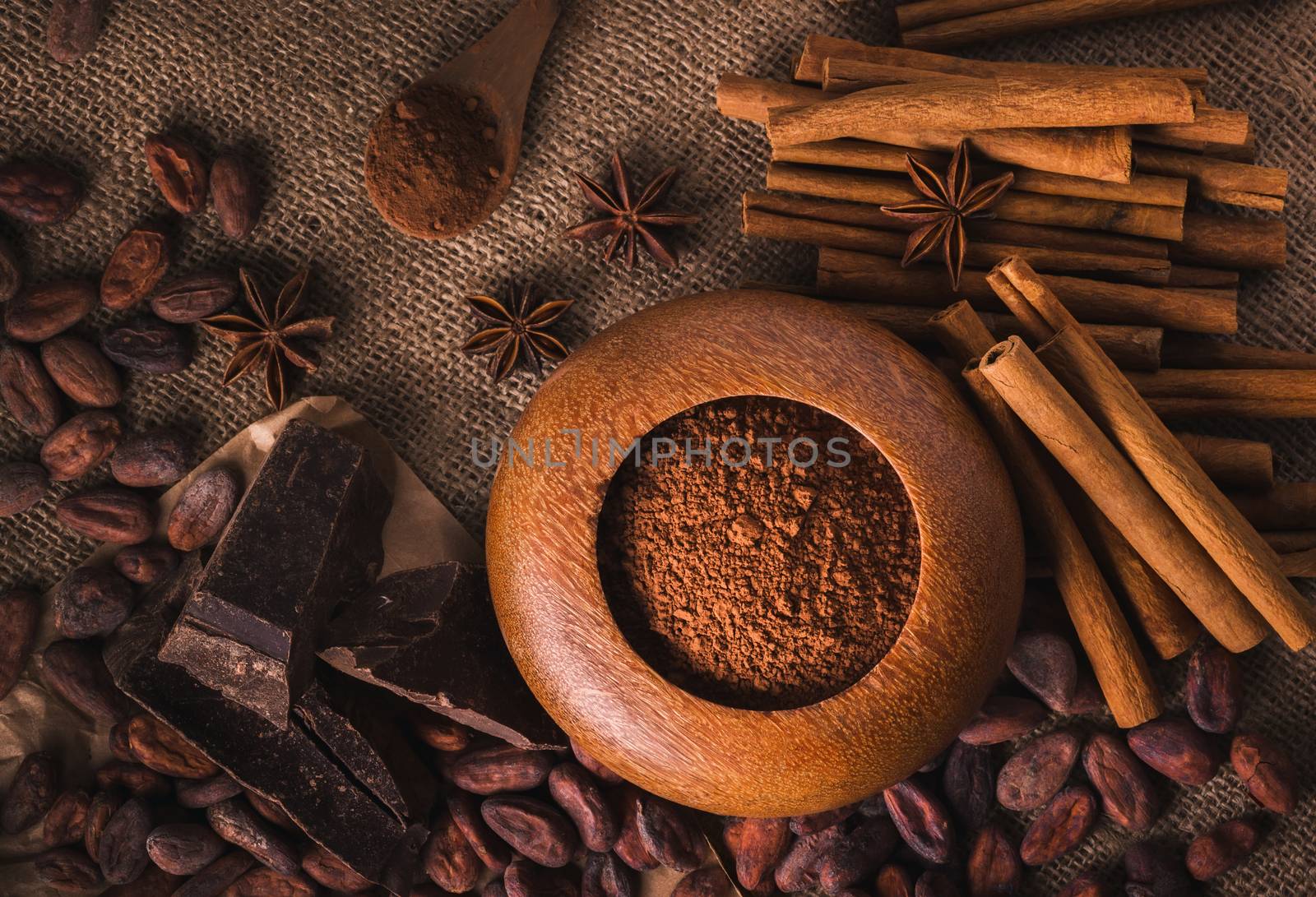 Raw cocoa beans, raw dark  homemade chocolate for raw foodists, cinnamon sticks, star anise and cocoa powder in a wooden bowl, top view