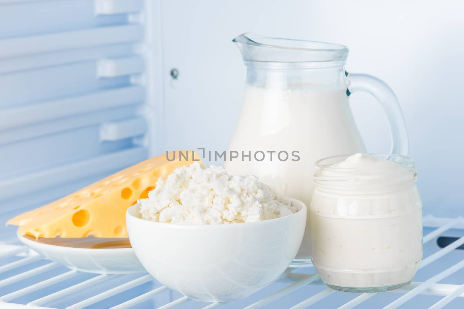 tasty healthy dairy products in the refrigerator: sour cream in the bank, cottage cheese in  bowl,  cheese  and milk in a jar