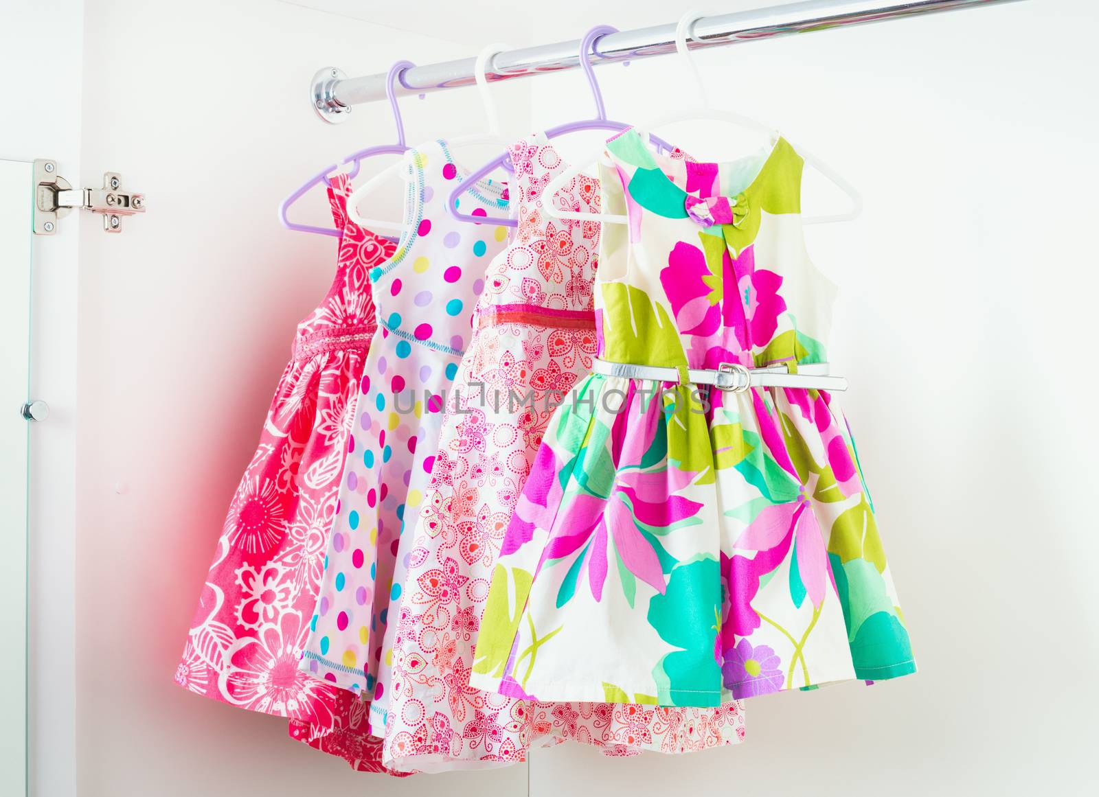 row of bright colorful little girl dresses hanging on coat hanger in white wardrobe