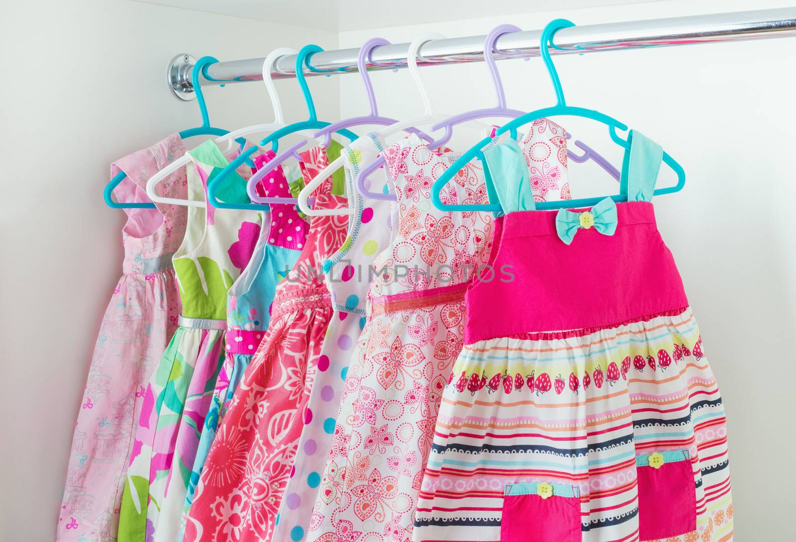 row of bright colorful little girl dresses hanging on coat hanger in white wardrobe