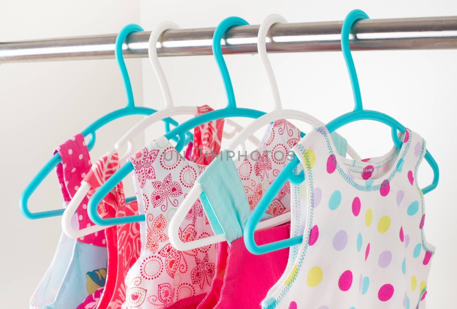 row of bright colorful little girl dresses hanging on coat hanger in white wardrobe