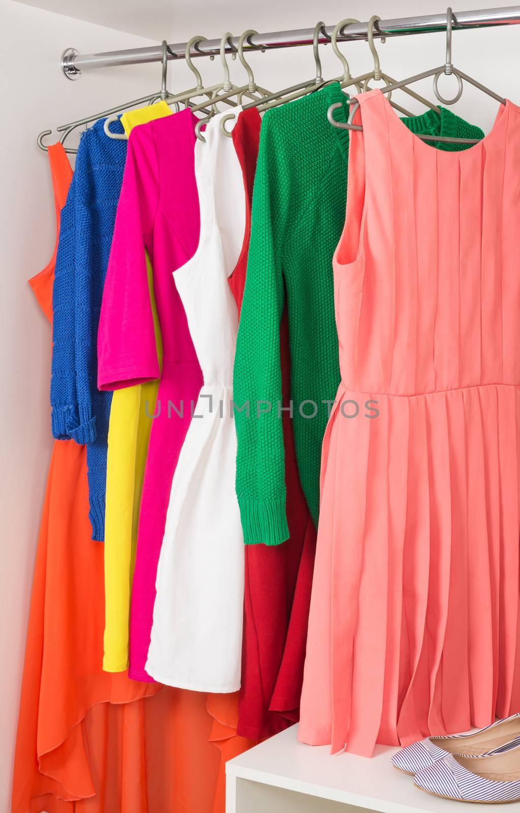 bright colorful female dresses and sweaters  hanging on coat hanger,  shoes and handbag in white wardrobe