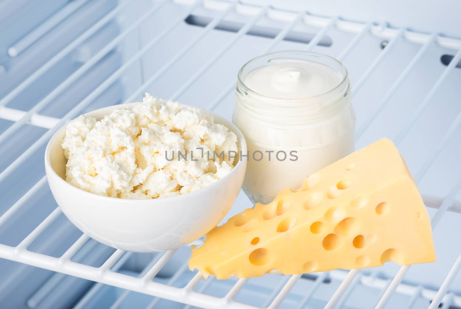 tasty and healthy dairy products on the shelf in the refrigerator: sour cream in the bank, cottage cheese in  bowl and slab of cheese 