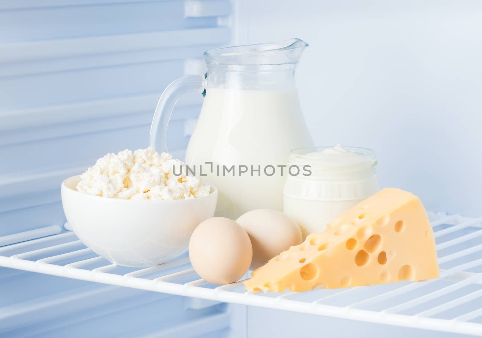 eggs and tasty healthy dairy products in the refrigerator: sour cream in the bank, cottage cheese in  bowl, eggs, cheese  and milk in a jar