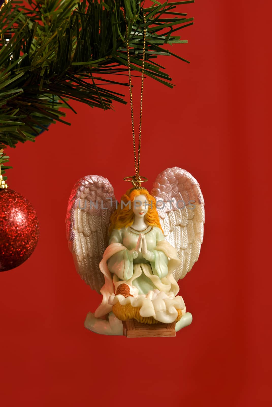 Vertical shot of a beautiful little angel ornament hanging on the Christmas tree shot on a red background.