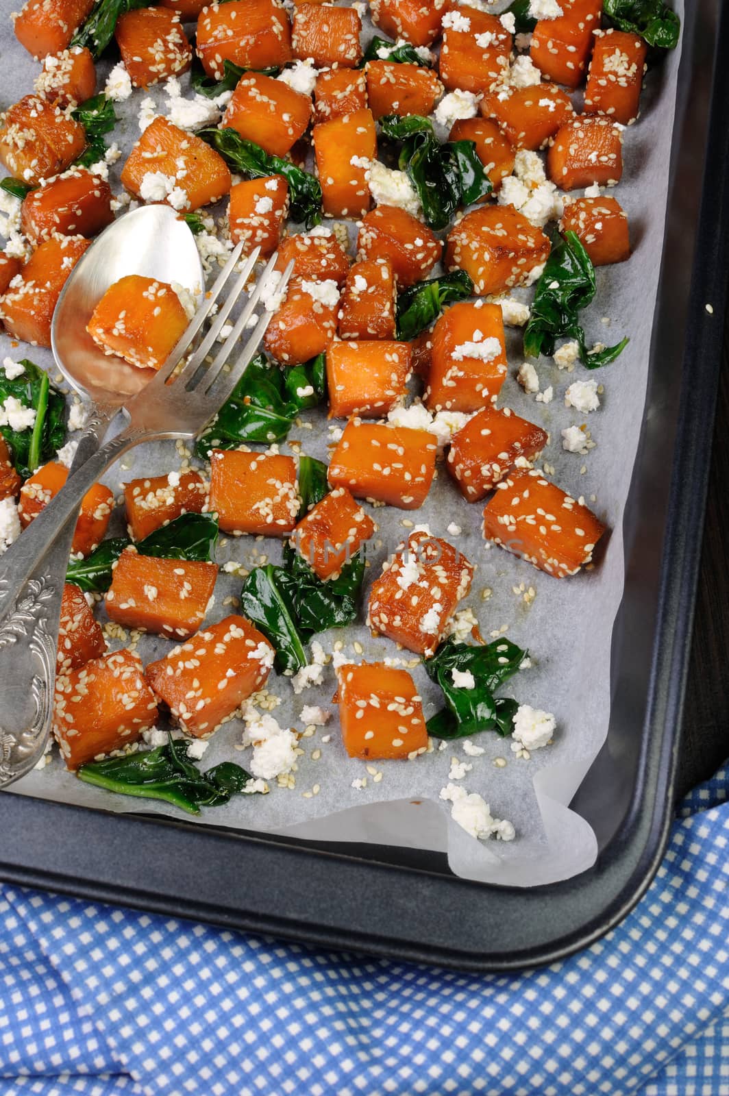 Slices of pumpkin baked with spinach and sesame seeds on a baking sheet