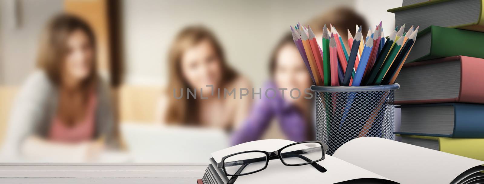 School supplies on desk against smiling friends students using laptop