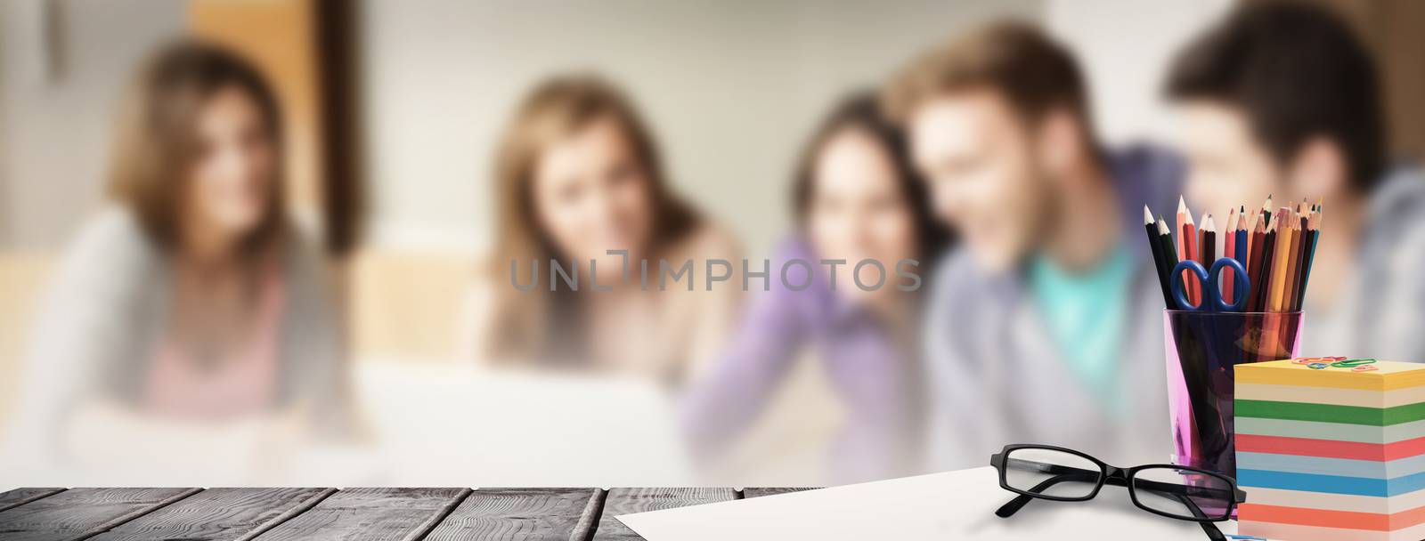 School supplies on desk against smiling friends students using laptop