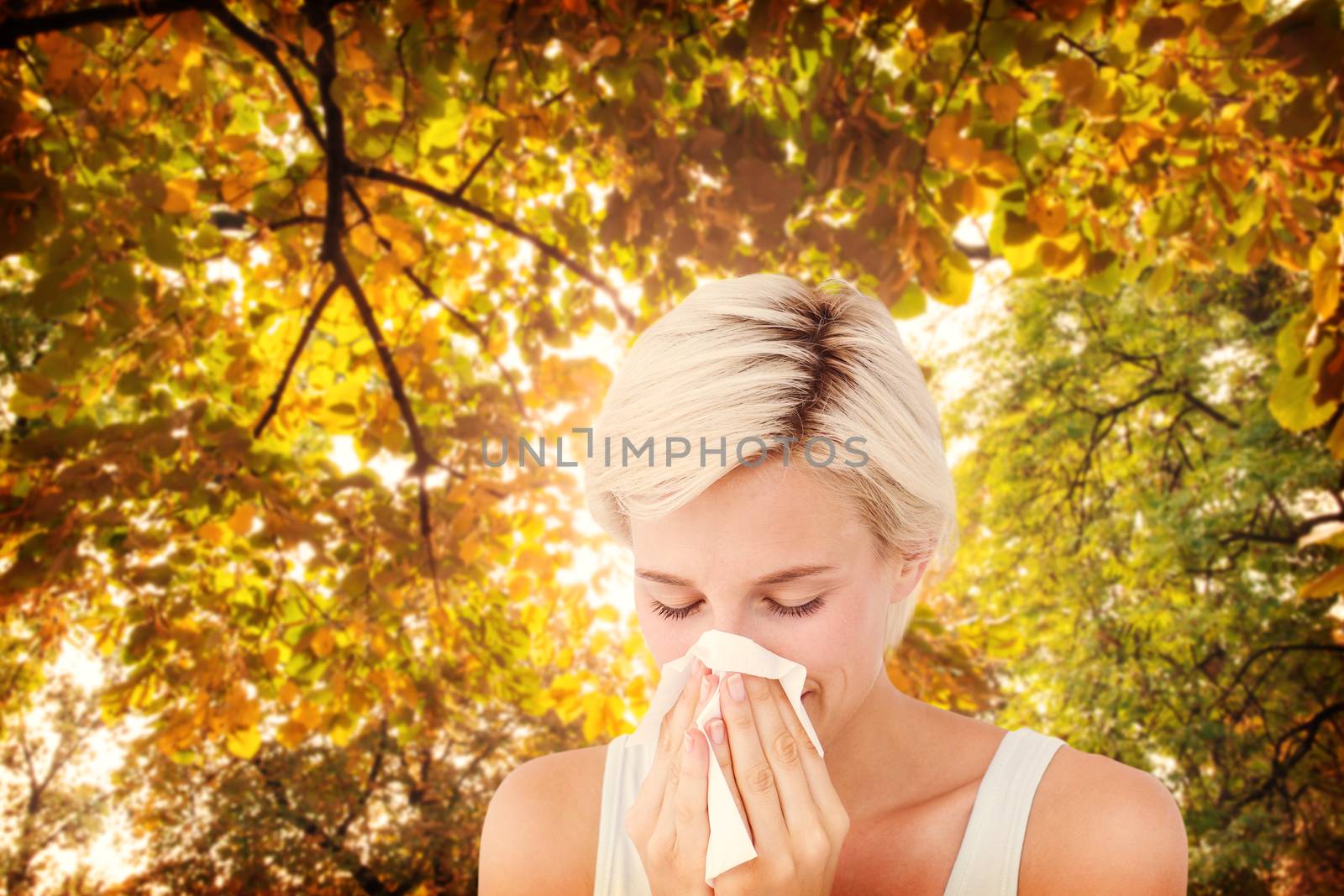 Sick woman blowing her nose against branches and autumnal leaves against the sunlight
