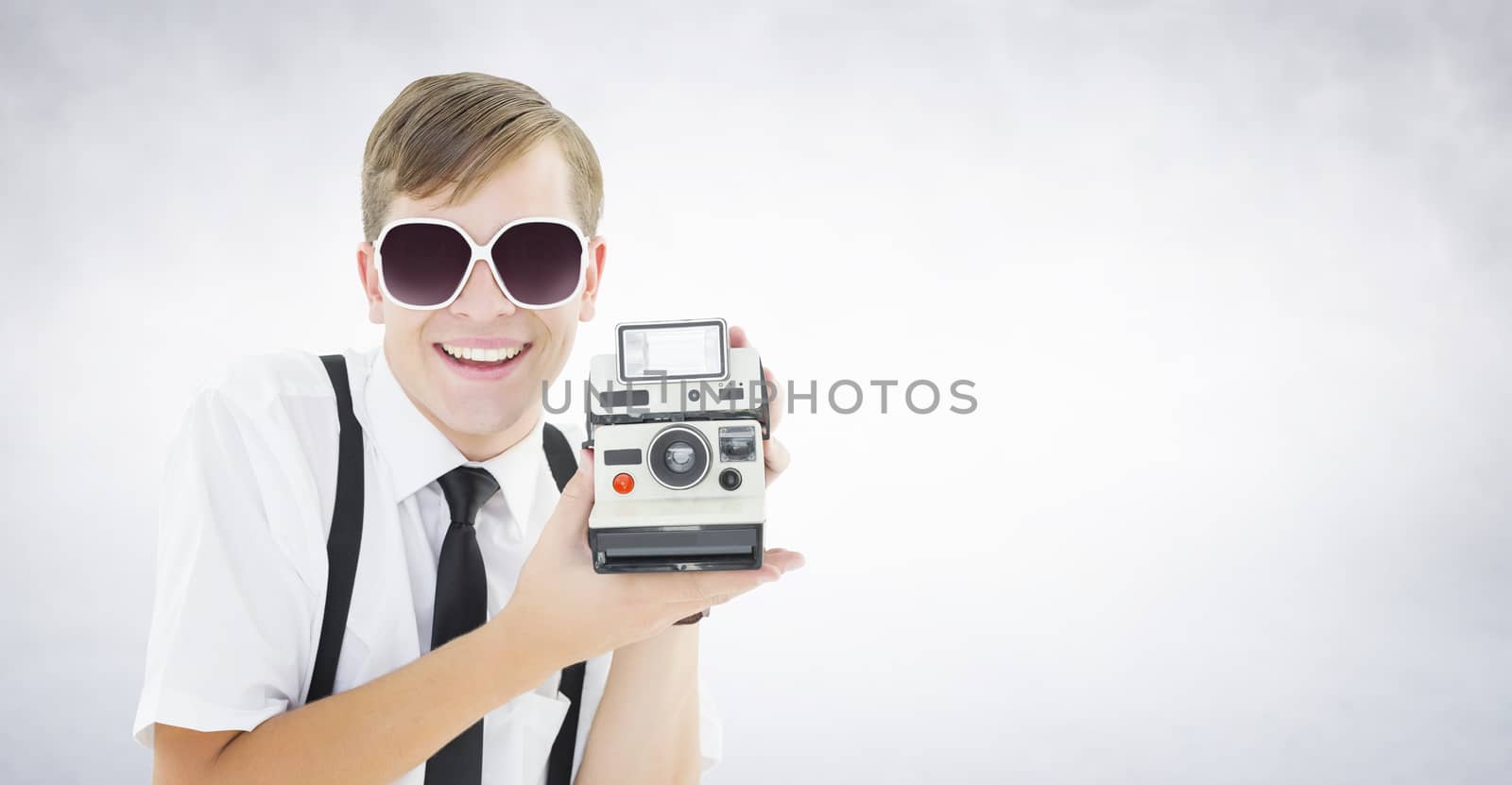 Geeky hipster holding a retro camera against white wall