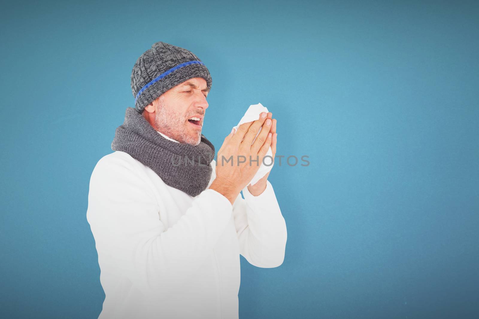 Sick man in winter fashion sneezing against blue background