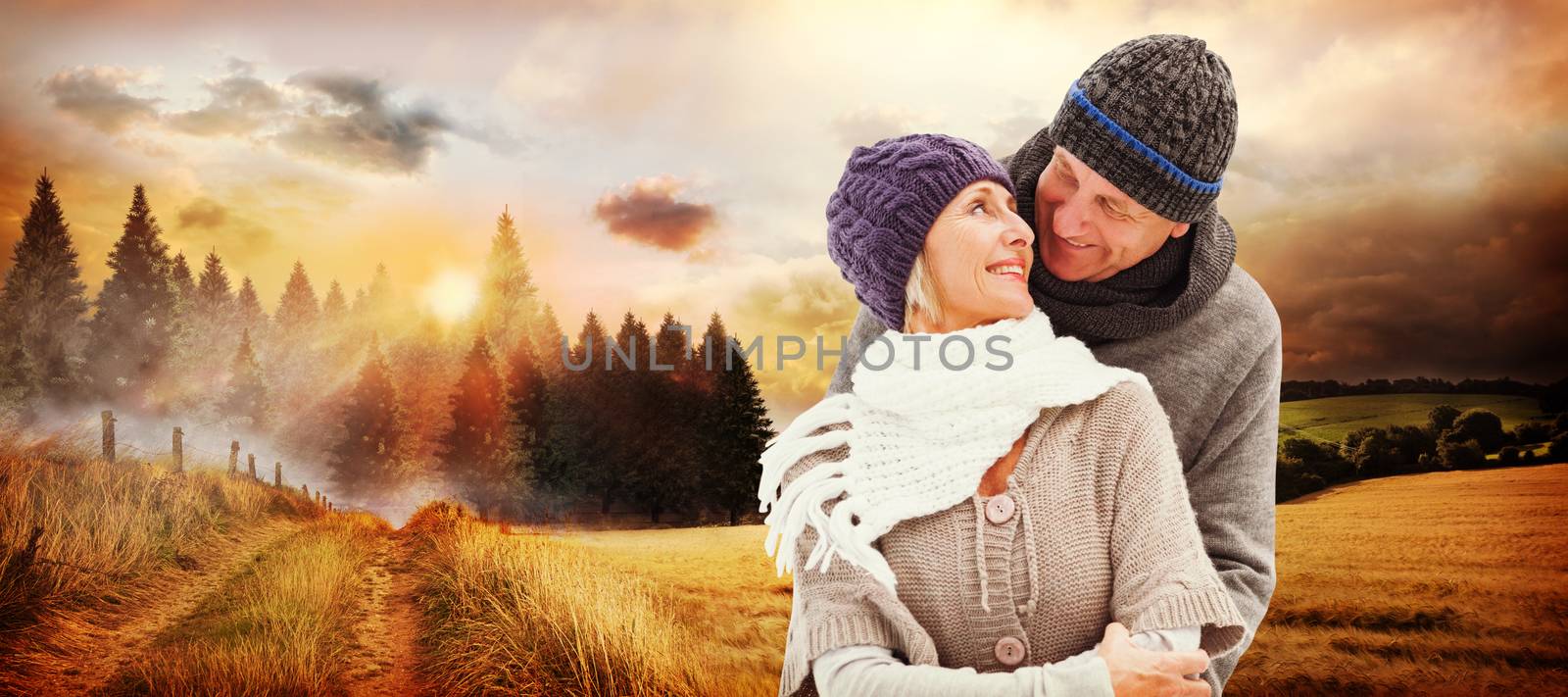 Happy mature couple in winter clothes embracing against country scene