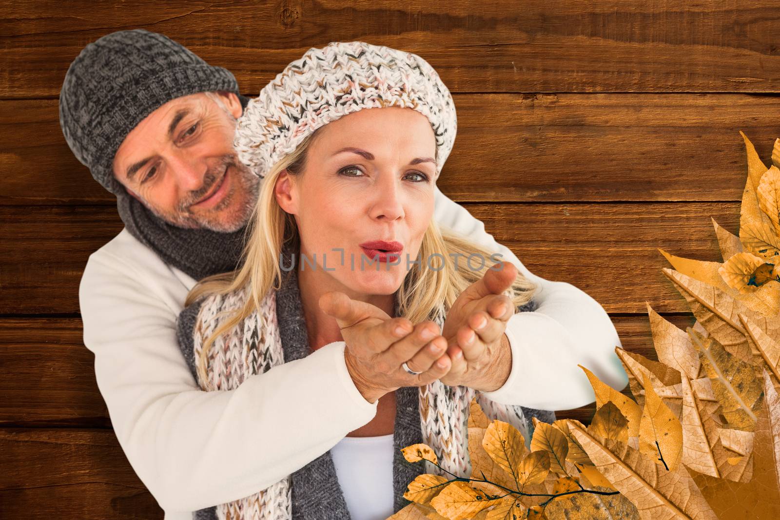 Husband hugging wife from behind as she blows kiss in air against overhead of wooden planks