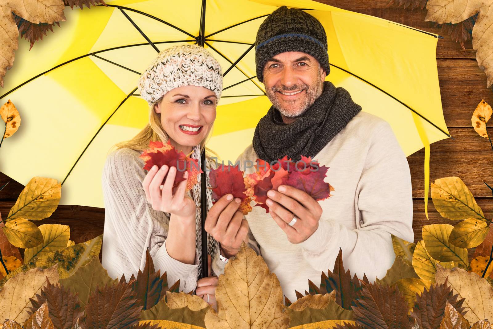 Portrait of couple holding autumn leaves while standing under yellow umbrella against overhead of wooden planks