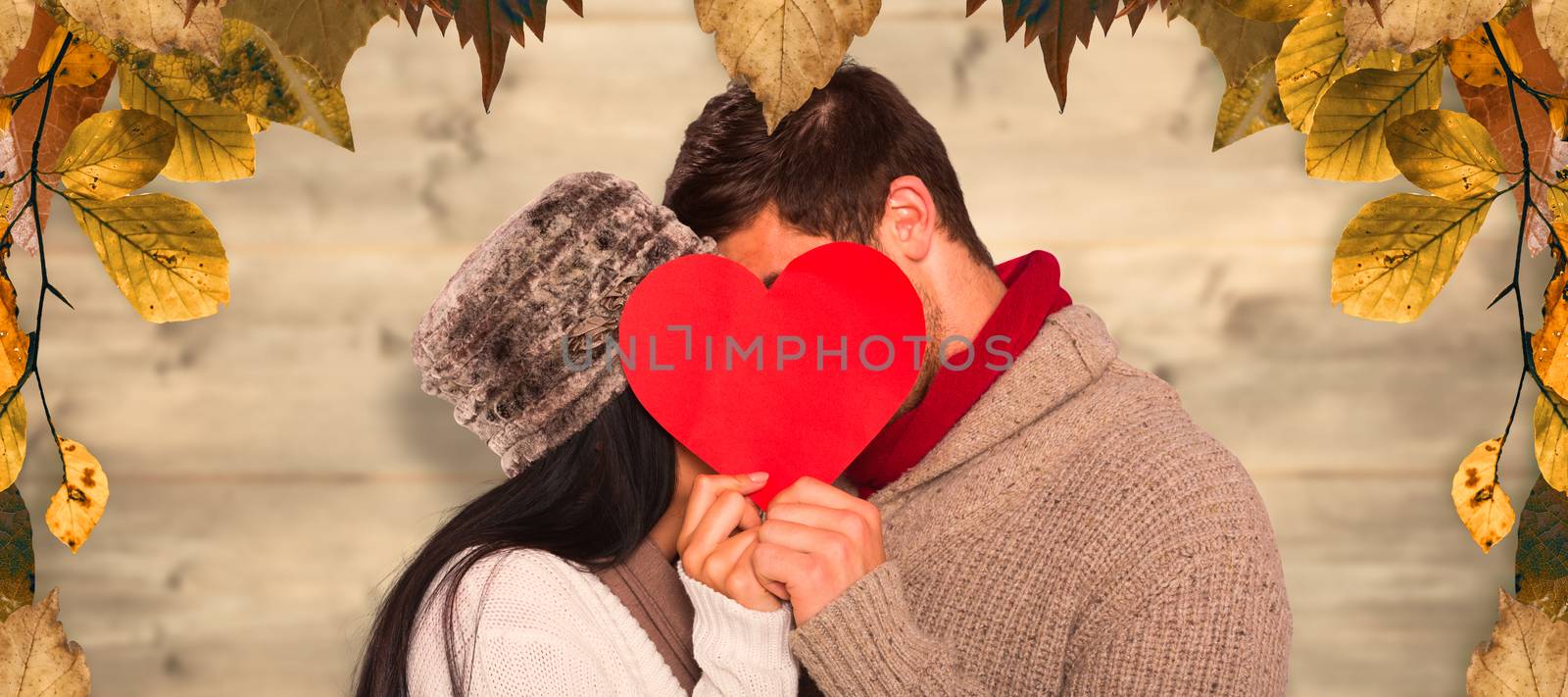 Young couple kissing behind red heart against bleached wooden planks background