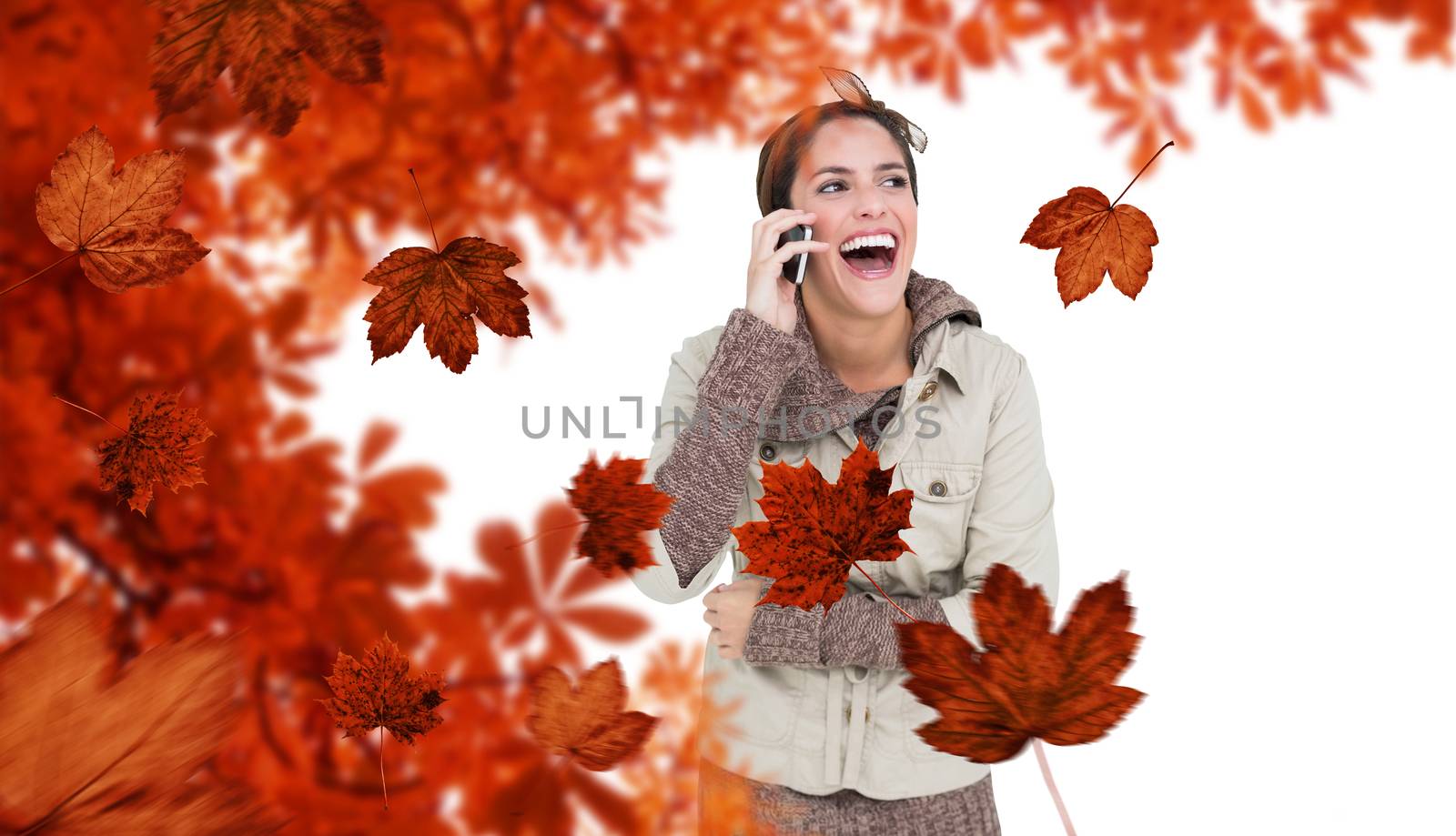 Laughing cute brunette in winter fashion phoning against autumn leaves pattern