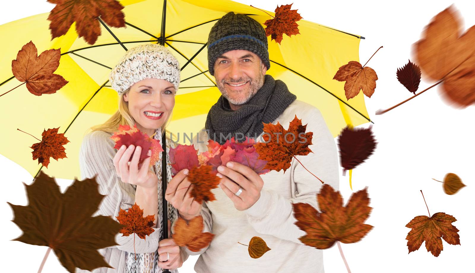 Composite image of portrait of couple holding autumn leaves while standing under yellow umbrella by Wavebreakmedia