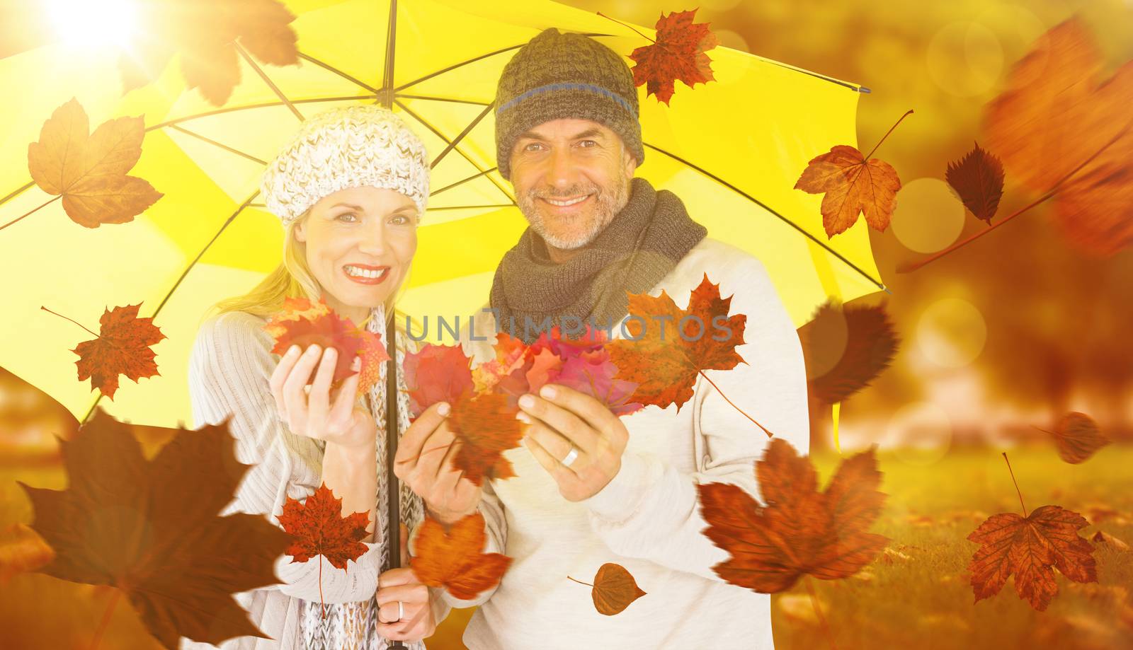 Portrait of couple holding autumn leaves while standing under yellow umbrella against park
