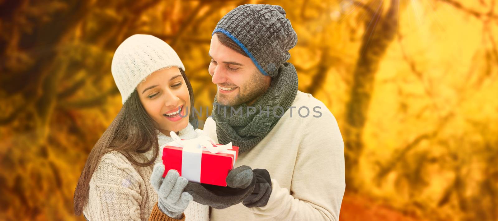 Winter couple holding gift against peaceful autumn scene in forest