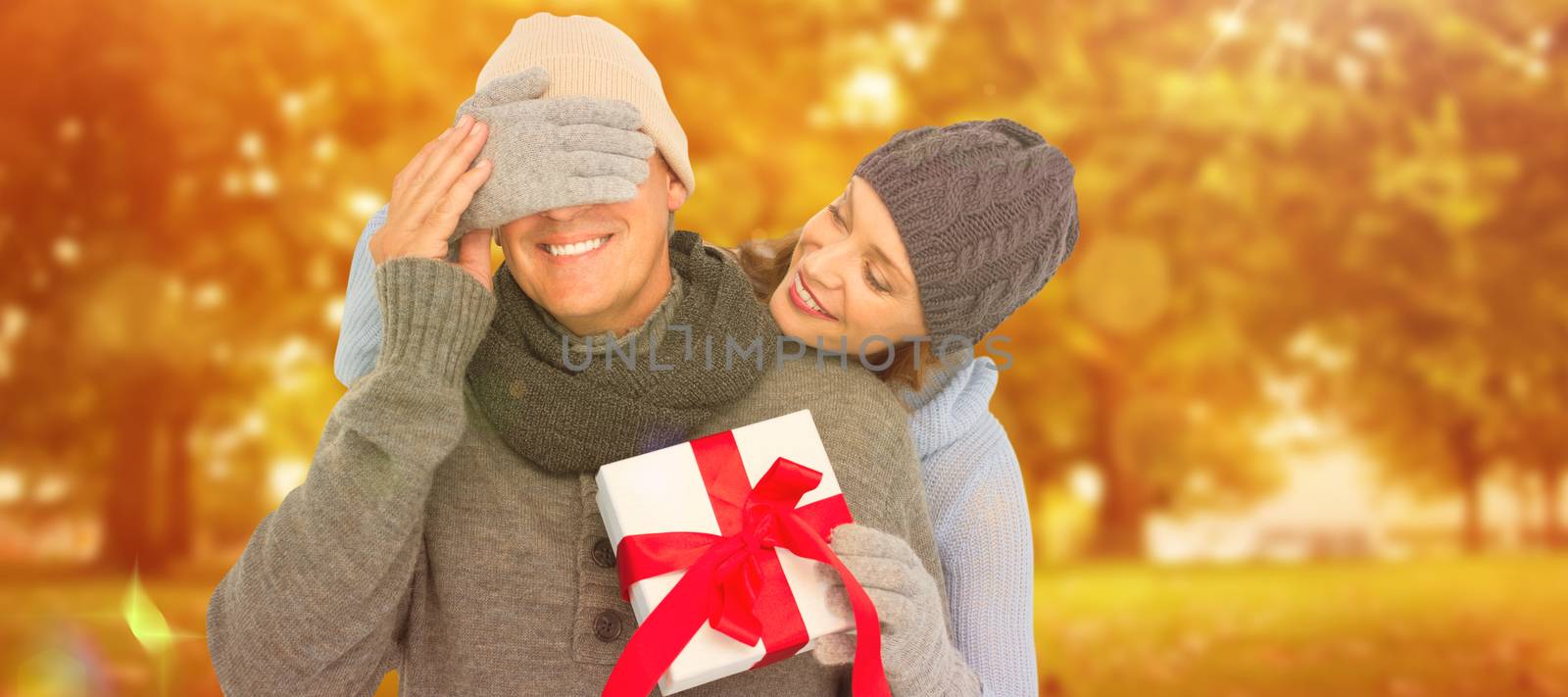 Woman surprising husband with gift against autumn scene