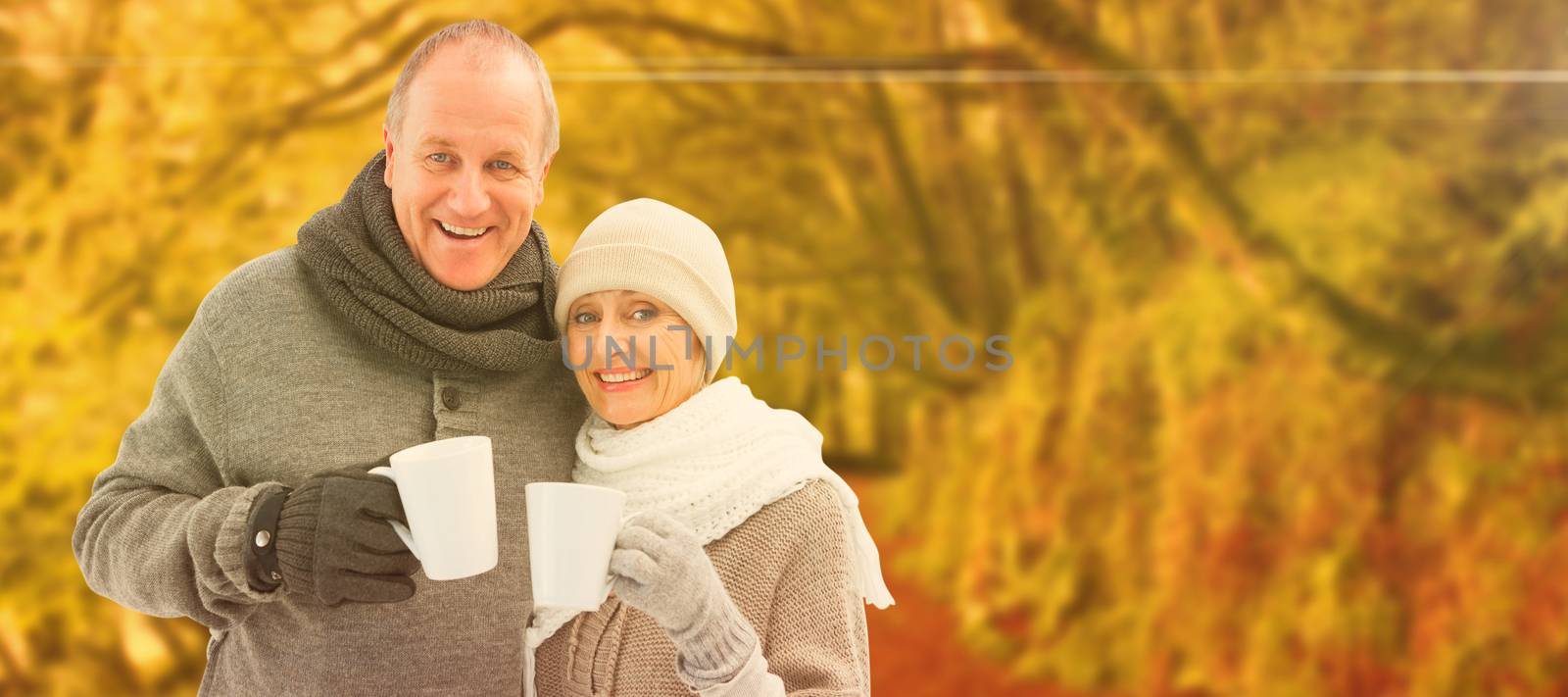 Happy mature couple in winter clothes holding mugs against peaceful autumn scene in forest