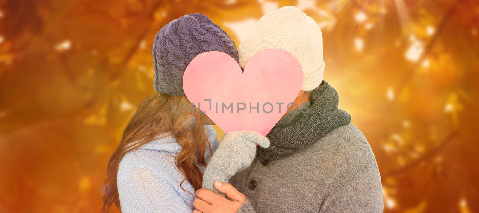 Couple in warm clothing holding heart against autumn scene