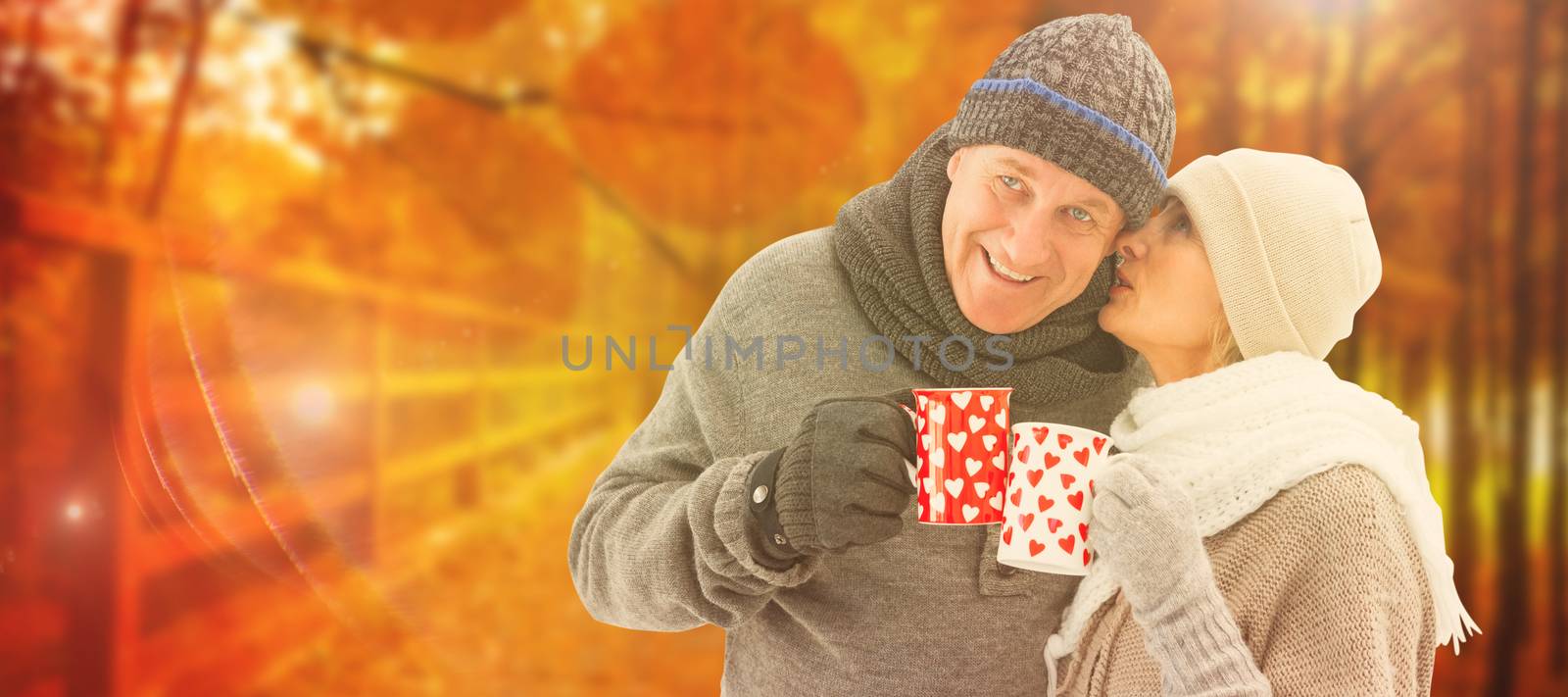 Happy mature couple in winter clothes holding mugs against autumn scene
