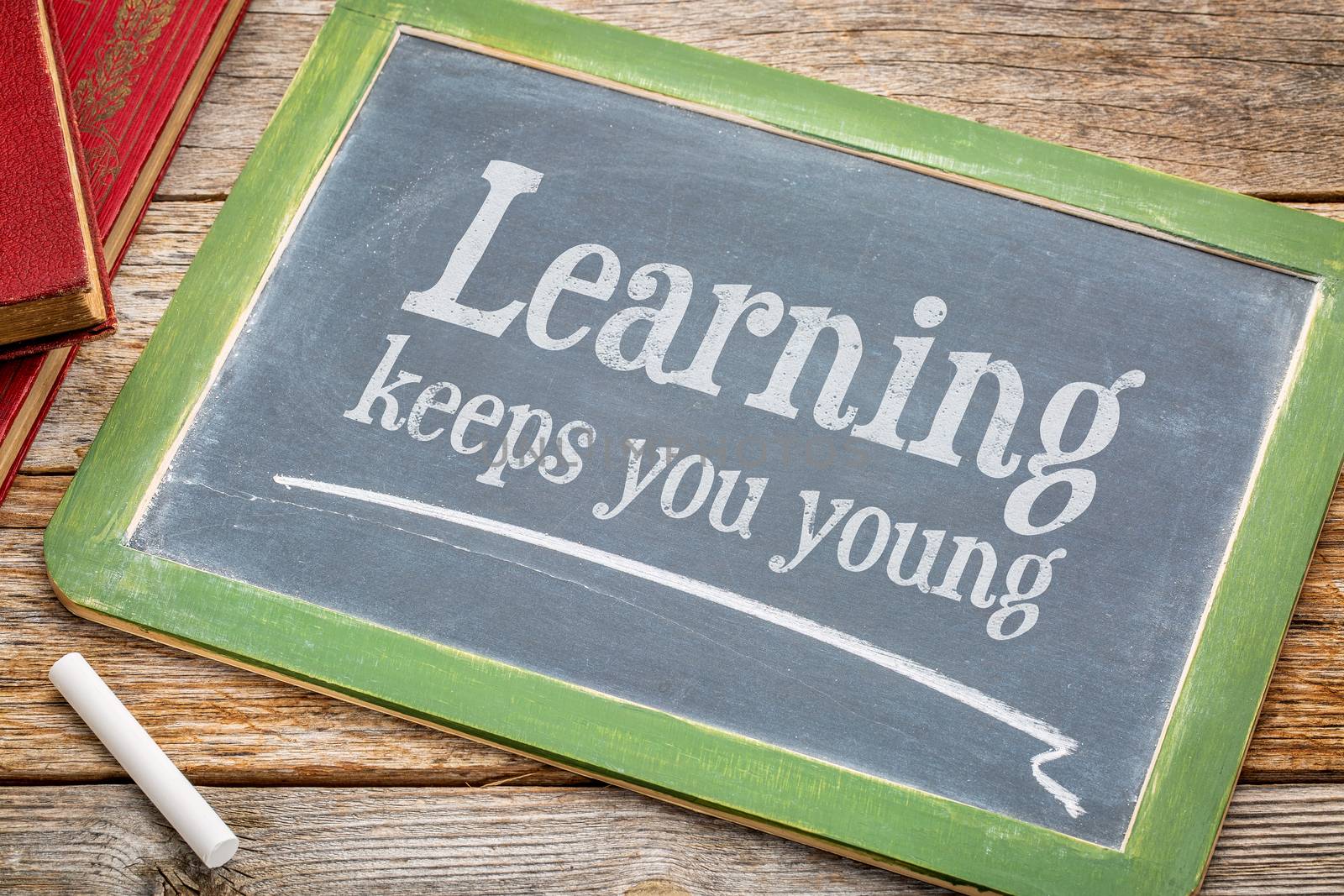 learning keeps you young - inspirationall words with a white chalk on a blackboard with a stack of books against rustic wooden table