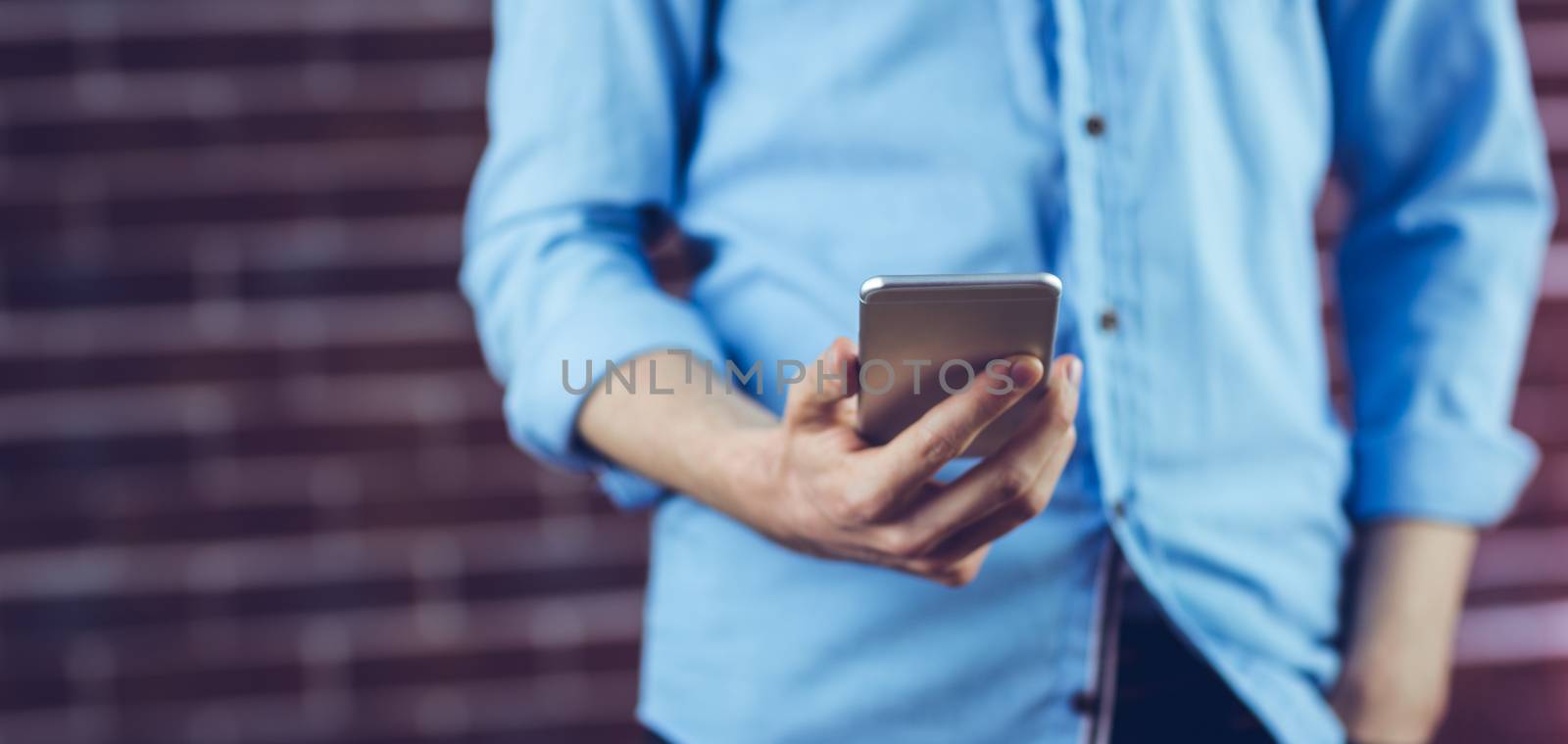 Midsection of man holding cellphone against brick wall