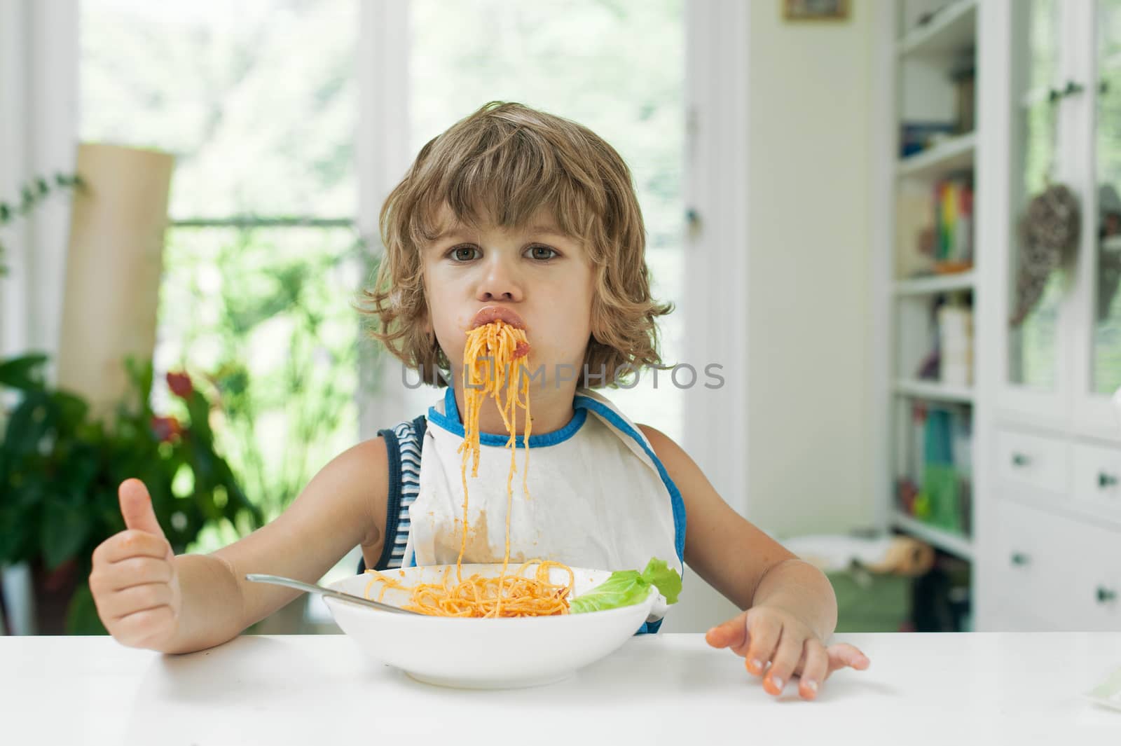 Portrait of a cute young boy making a mess while eating pasta for lunch. Bad manners concept.