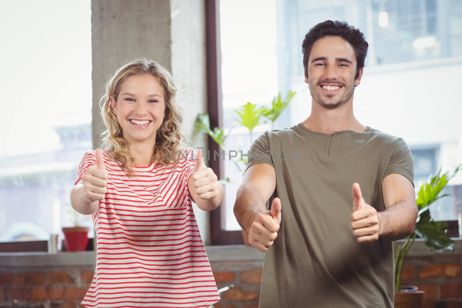Business people giving thumbs up in creative office