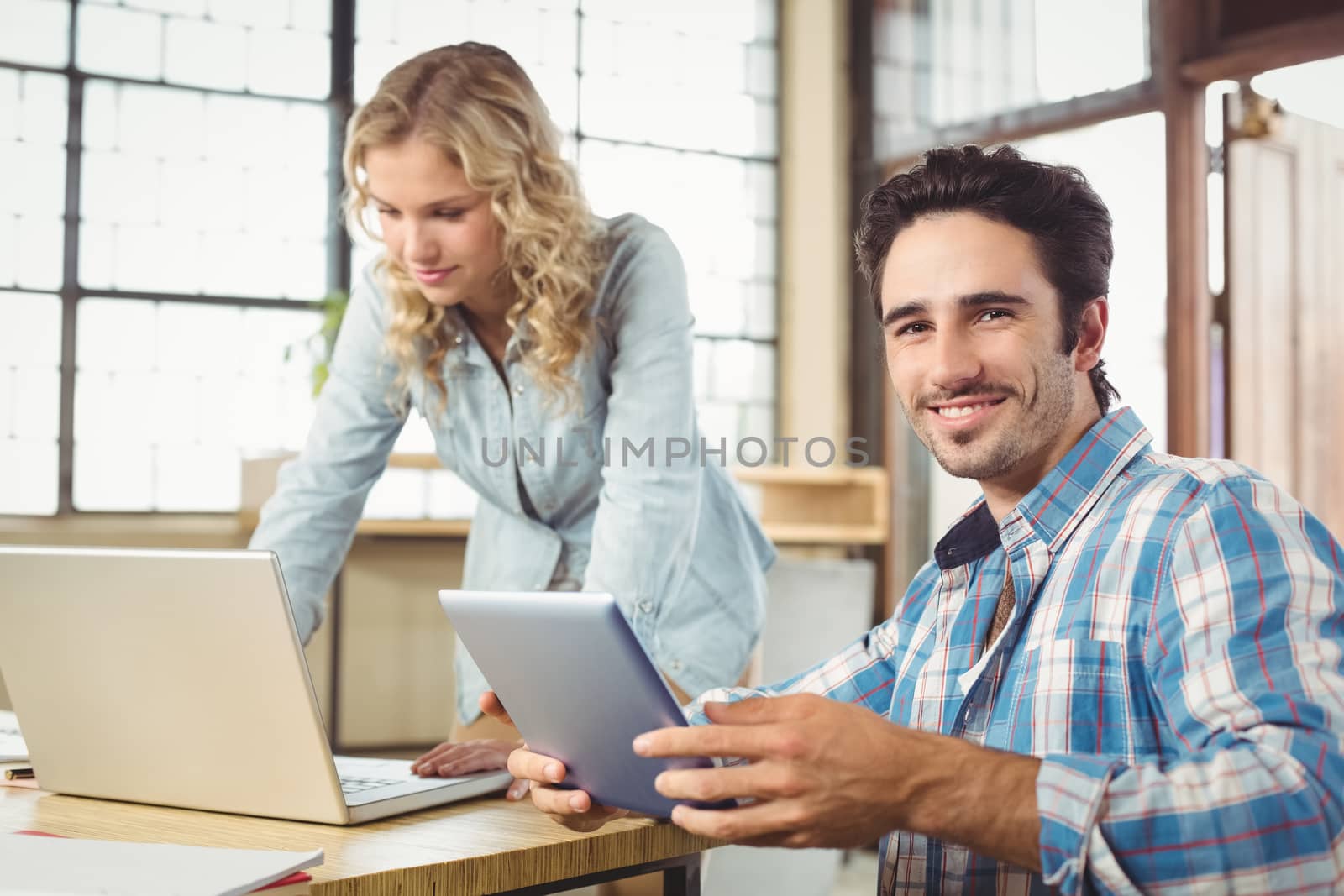 Portrait of smiling  man holding tablet with woman working in office 