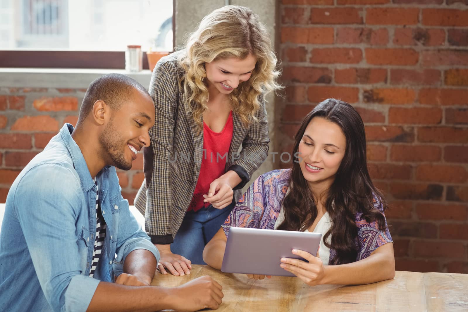 Smiling business people discussing over tablet in creative bright office