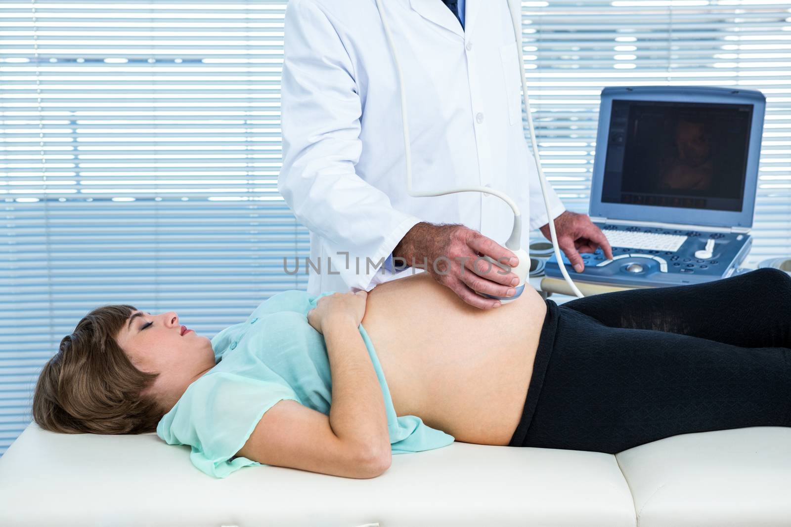 Midsection of male doctor performing ultrasound on pregnant woman