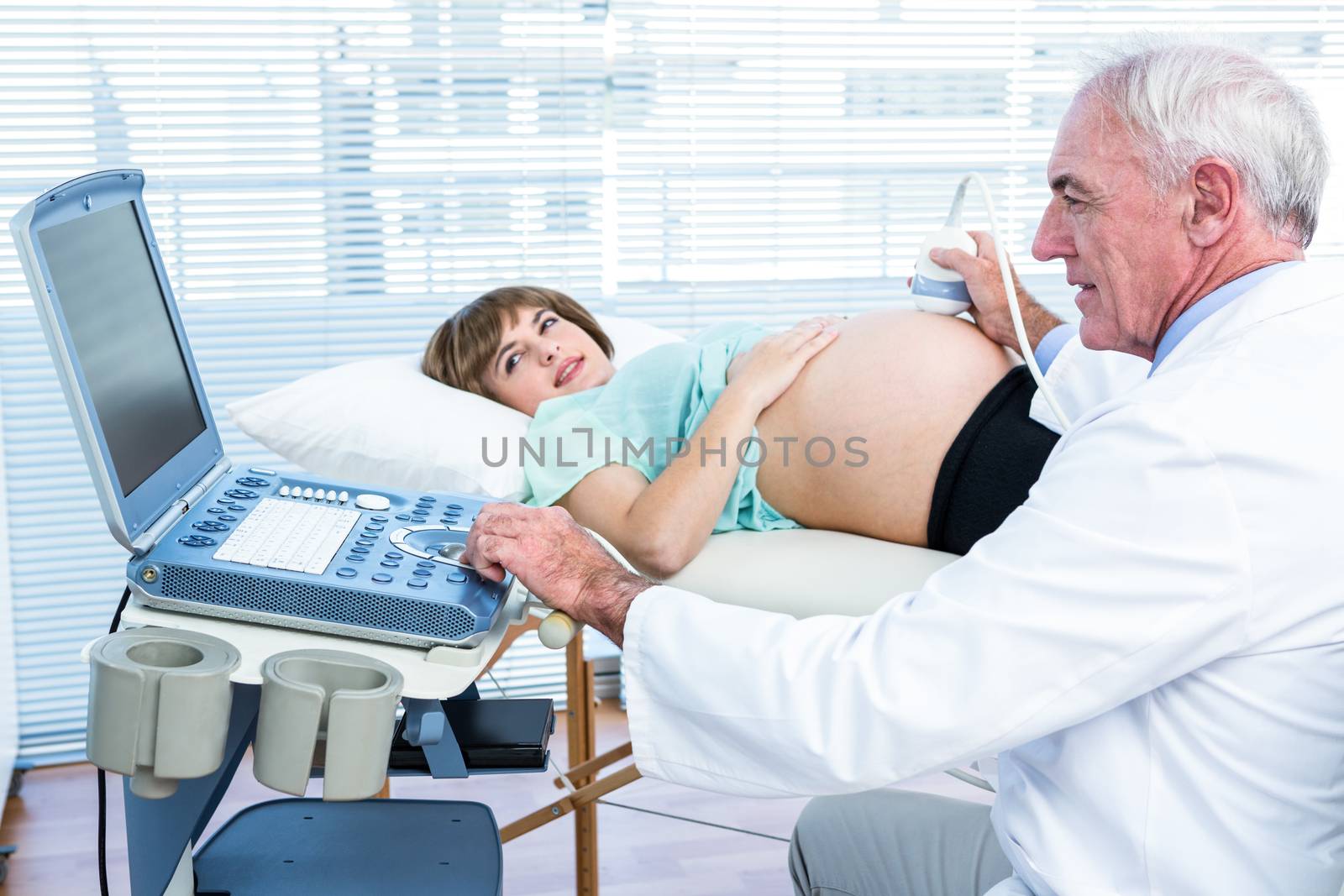 Pregnant woman and doctor looking at scan machine while performing ultrasound test
