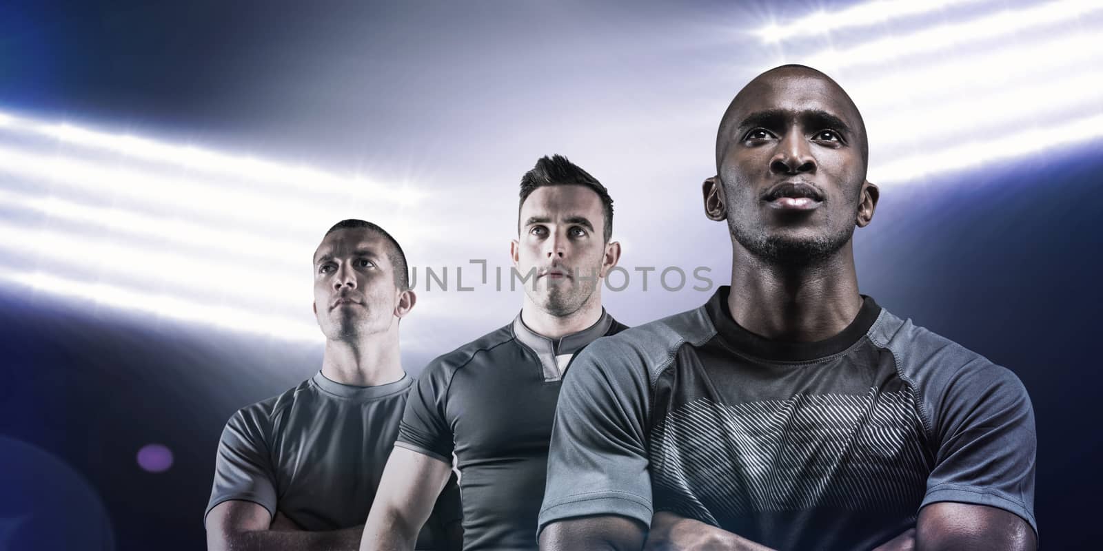 Thoughtful athlete standing with arms crossed against spotlights