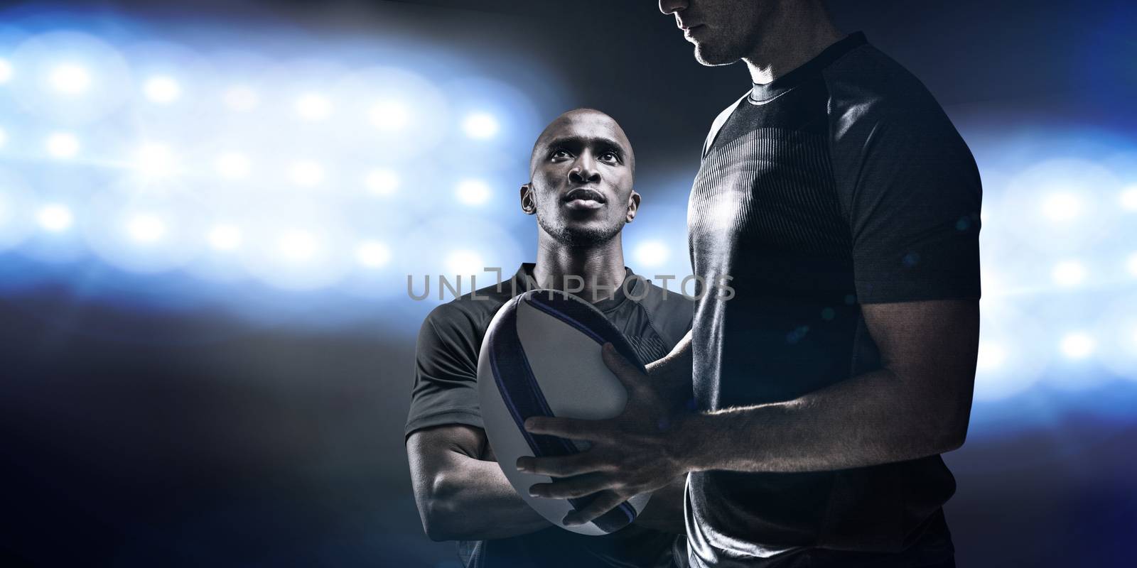 Calm rugby player thinking while holding ball against spotlights