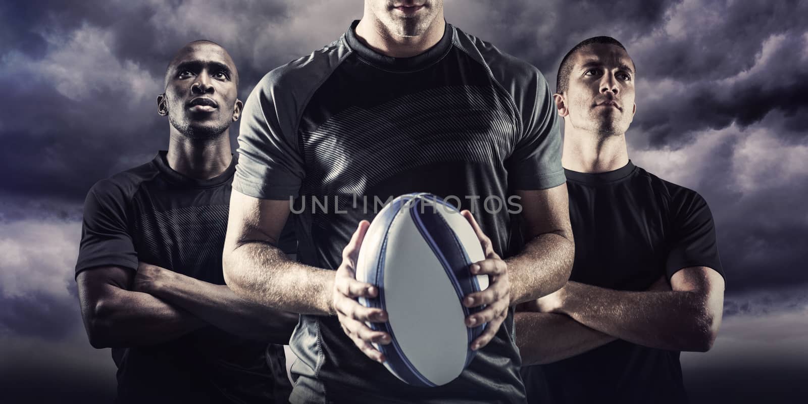 Thoughtful rugby player holding ball against blue sky