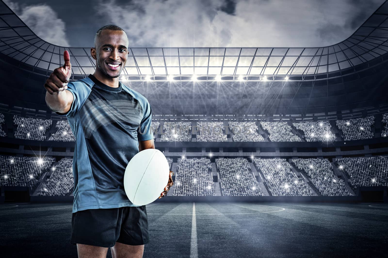 Portrait of confident rugby player smiling and showing thumbs up against large football stadium under spotlights